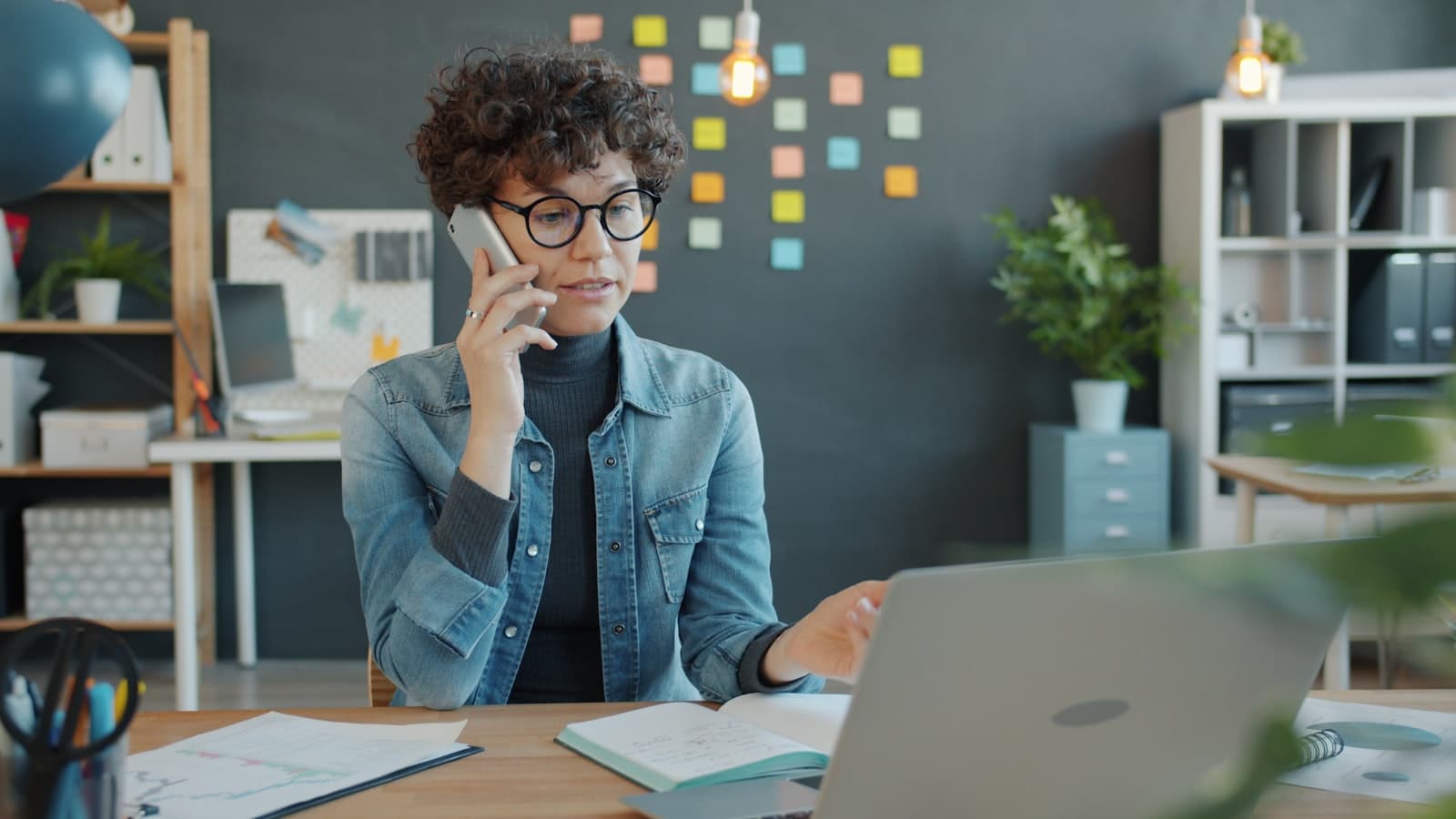 A woman on a phone call at a desk with a laptop.