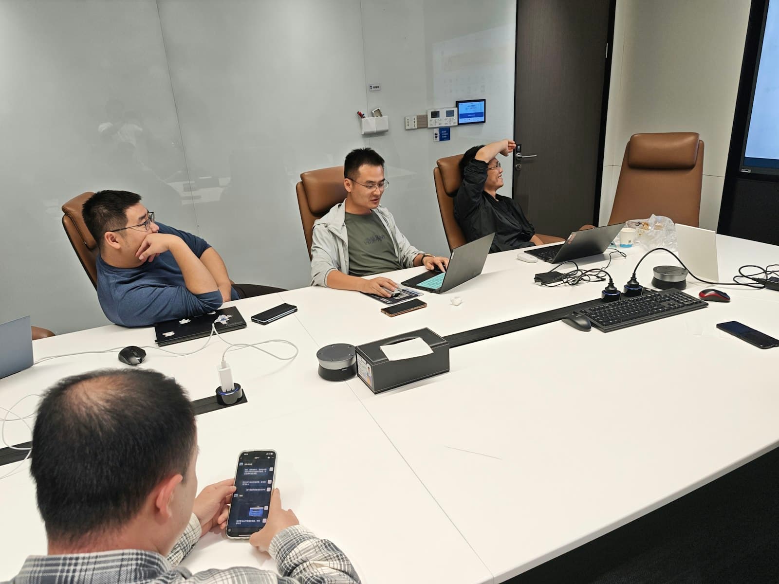 Four people in a meeting room, laptops open.