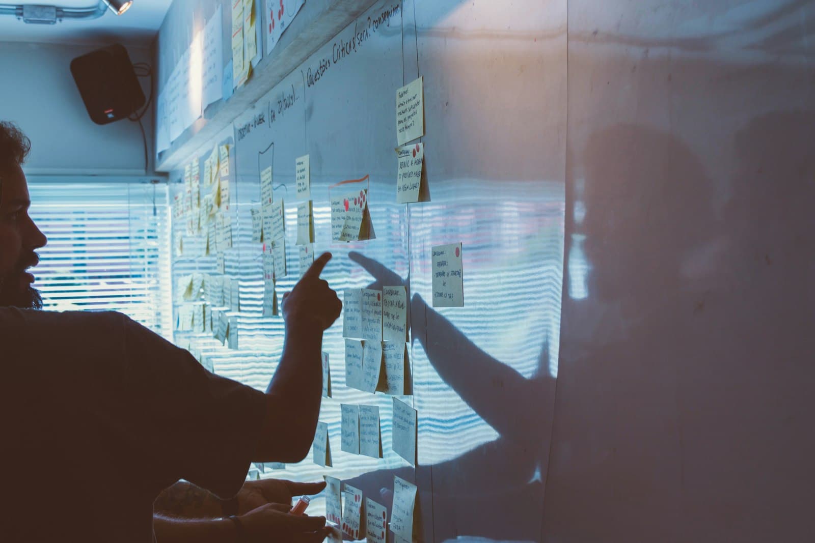 A person pointing at notes pinned on a wall during a team session.